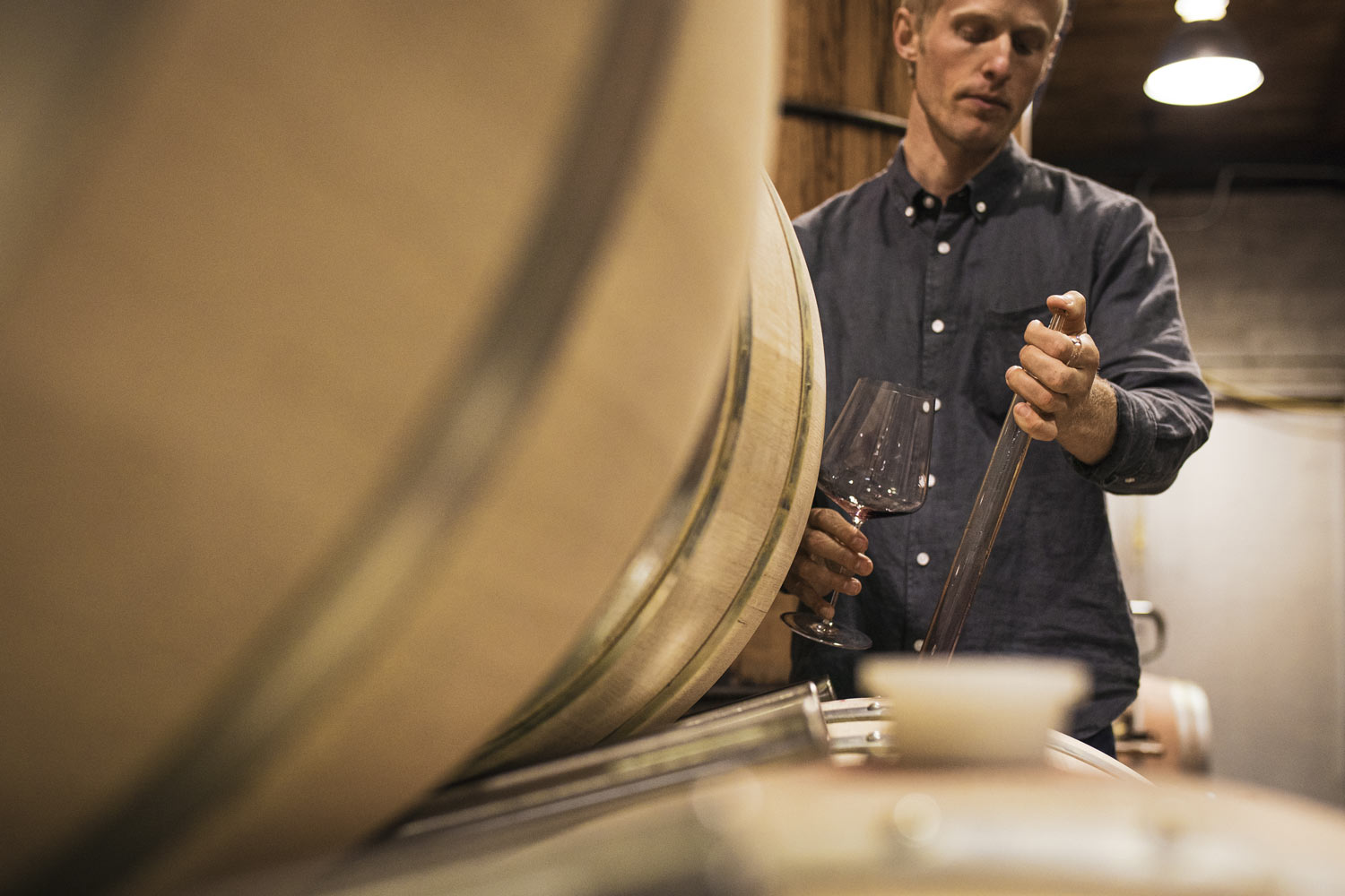 Close-up of winemaking team member taking a sample out of a barrel.