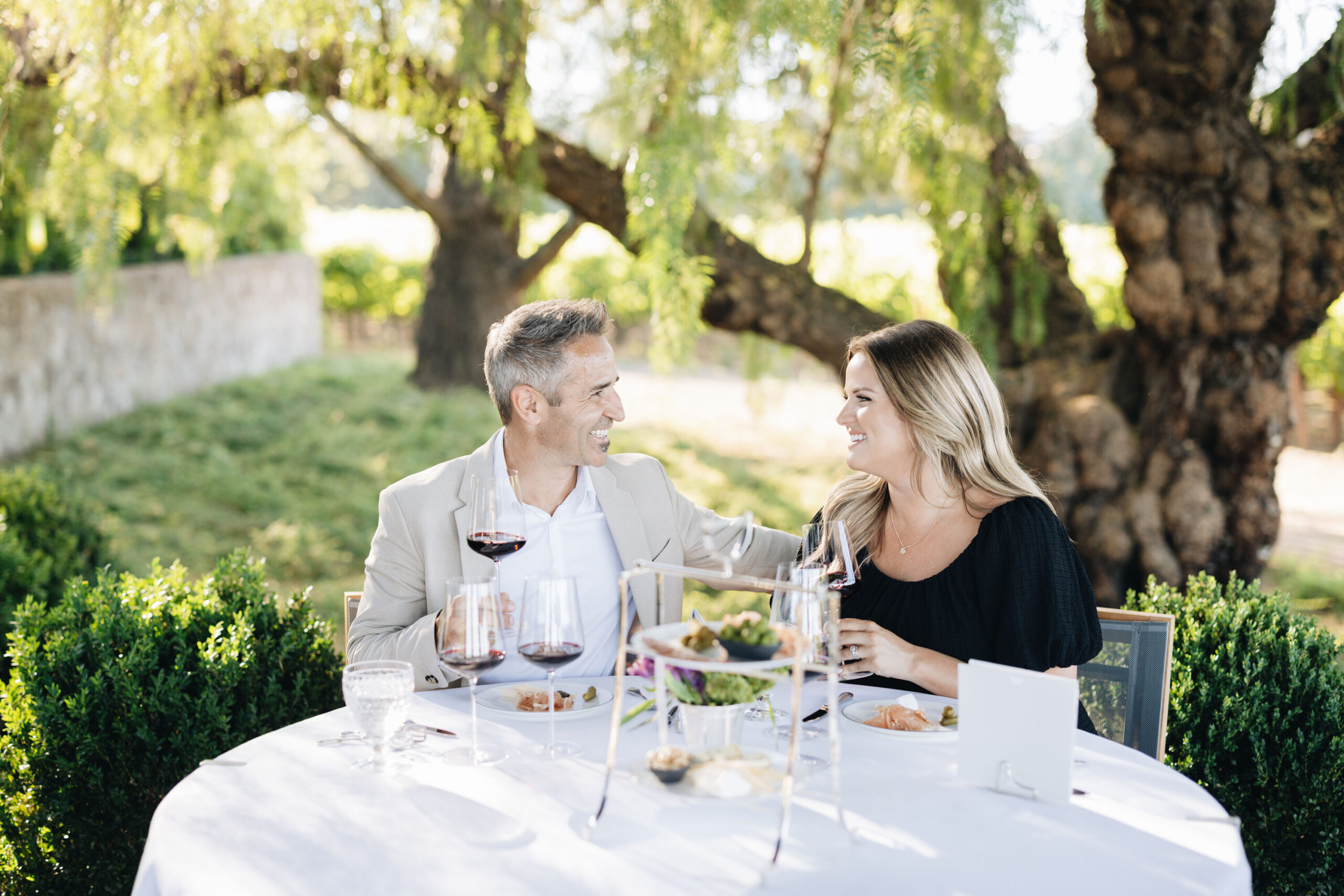 A couple enjoying a tasting outdoors at a table with glasses of wine and selection of cheese and meats on a plate at Heitz Cellar.