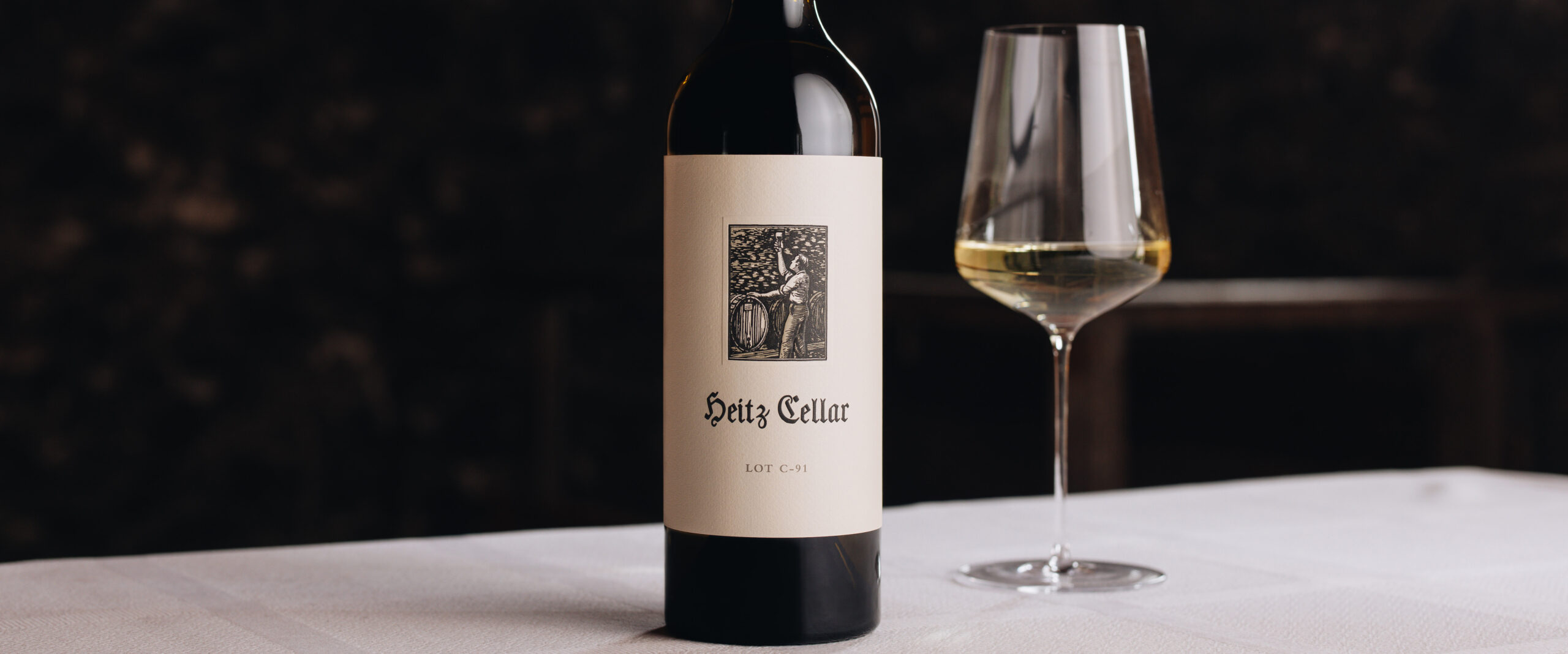 A bottle of Heitz Cellar Lot C-91 Blanc de Blanc next to a glass of white wine on a table.
