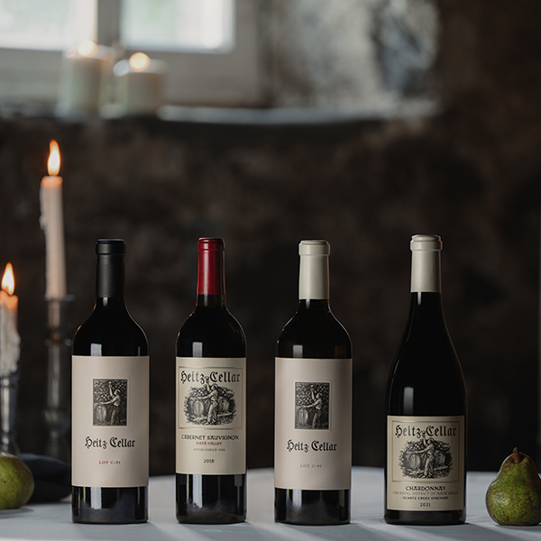 The Complete Table: a selection of Heitz Cellar bottles on a table including the 2019 Lot-C91 Cabernet Sauvignon, 2018 Napa Valley Cabernet Sauvignon, 2021 Lot-C-91 Sauvignon Blanc, 2021 Quartz Creek Chardoonay, with candles in the background.