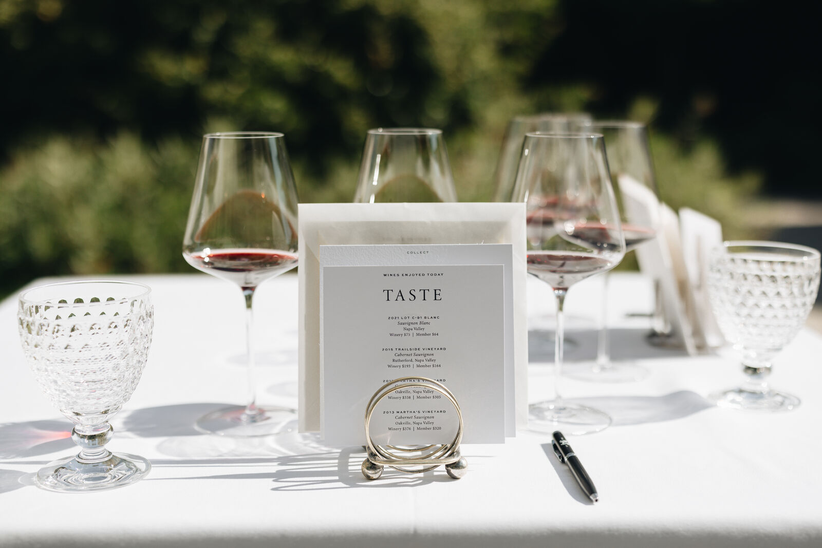 The Estate Legacy tasting: A table set with wine glasses outdoors and a tasting menu with a pen at The Estate at Heitz Cellar.