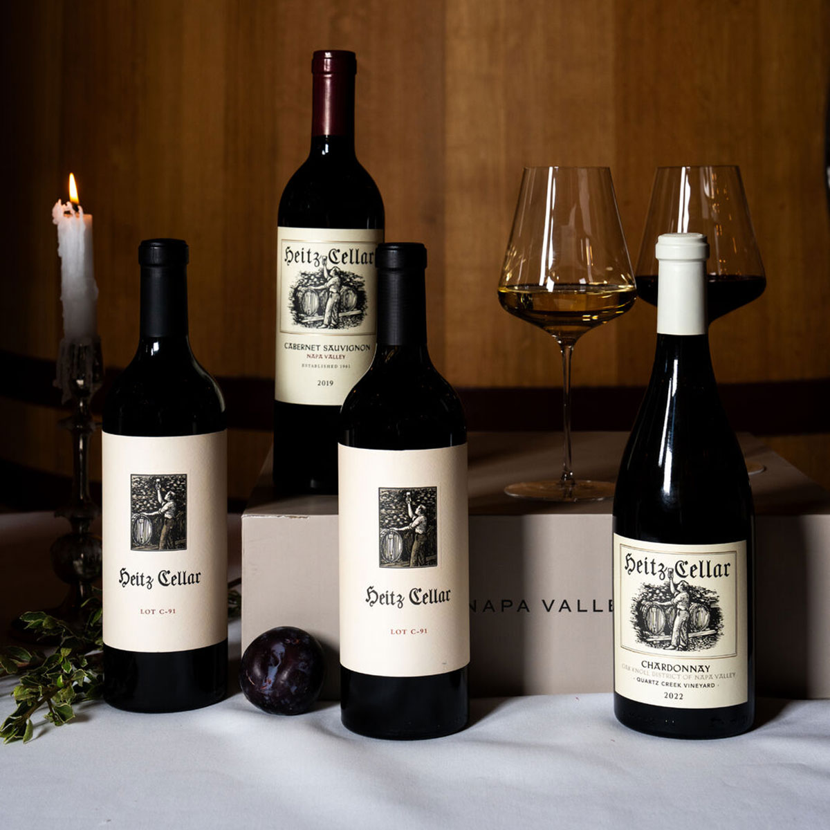 The Complete Table: a selection of Heitz Cellar bottles on a table including the 2019 Lot-C91 Cabernet Sauvignon, 2019 Napa Valley Cabernet Sauvignon, 2022 Lot-C-91 Sauvignon Blanc, 2022 Quartz Creek Chardonnay, with candles in the background.