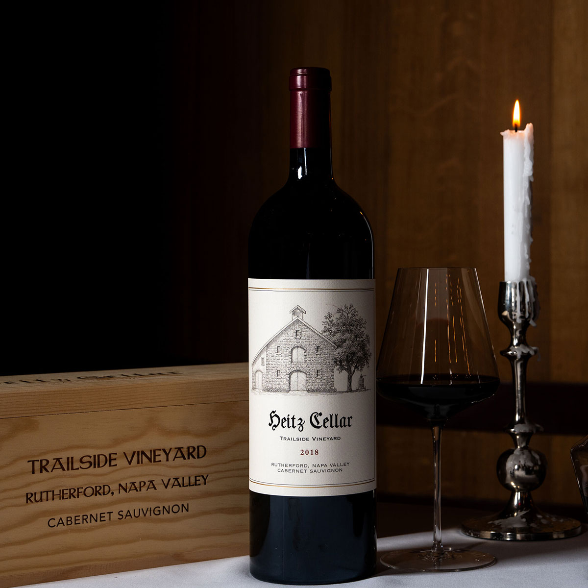 A bottle of Heitz Cellar 2018 Trailside Cabernet Sauvignon 1.5L (magnum) on a table with a glass of wine and a Trailside Wooden Box.